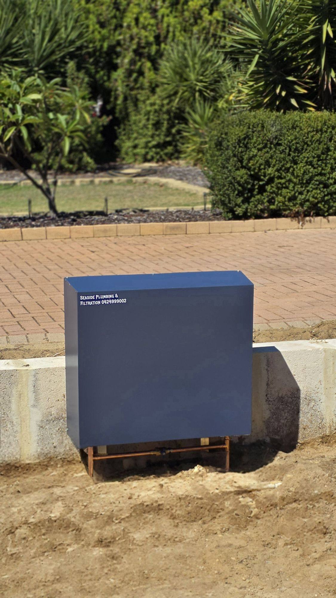 A blue-grey filter cover mounted in front of a low garden wall beside brick paving