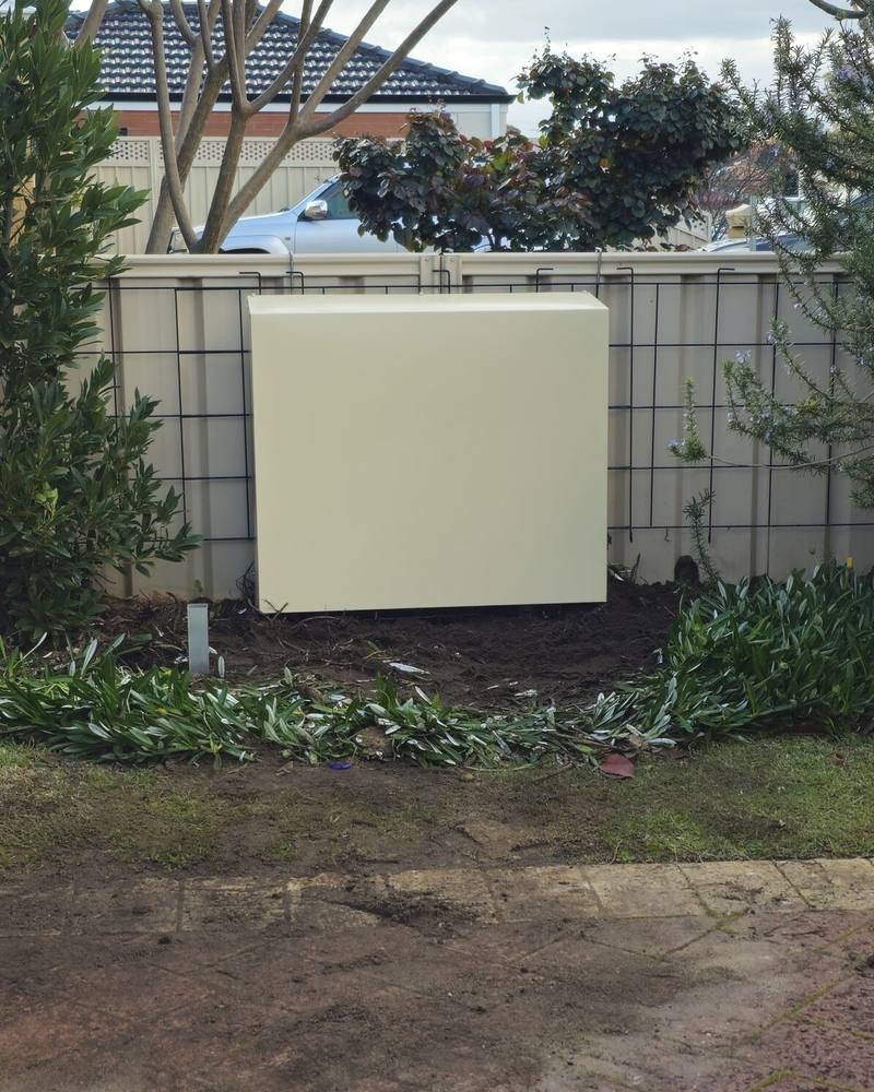 A cream filter cover on a side wall beside a fence, with new paving in front