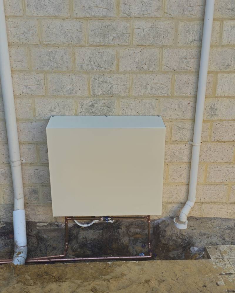 A cream filter cover on a cream brick wall, freshly installed between two downpipes