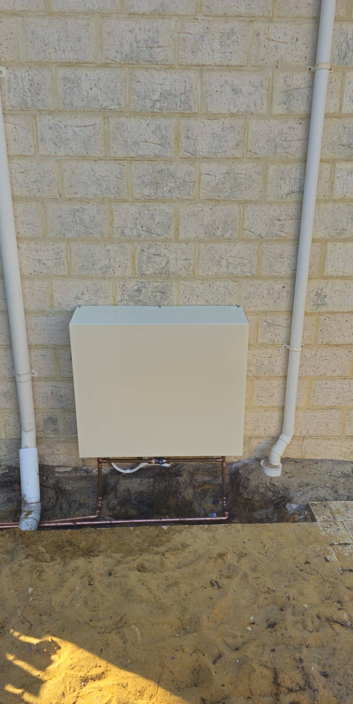 A cream filter cover on a cream brick wall, freshly installed between two downpipes