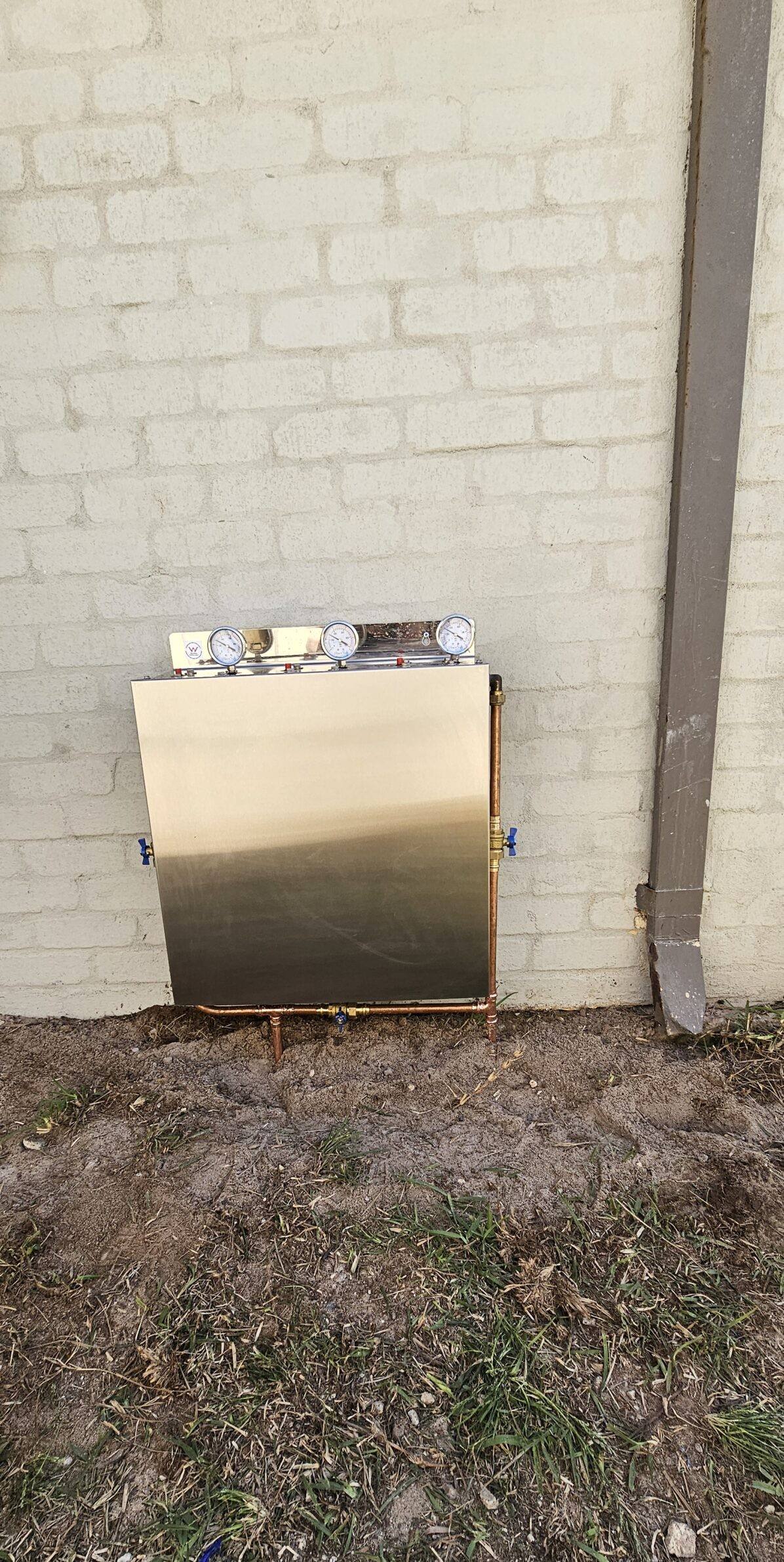 A stainless steel filter cover fitted to a cream brick wall
