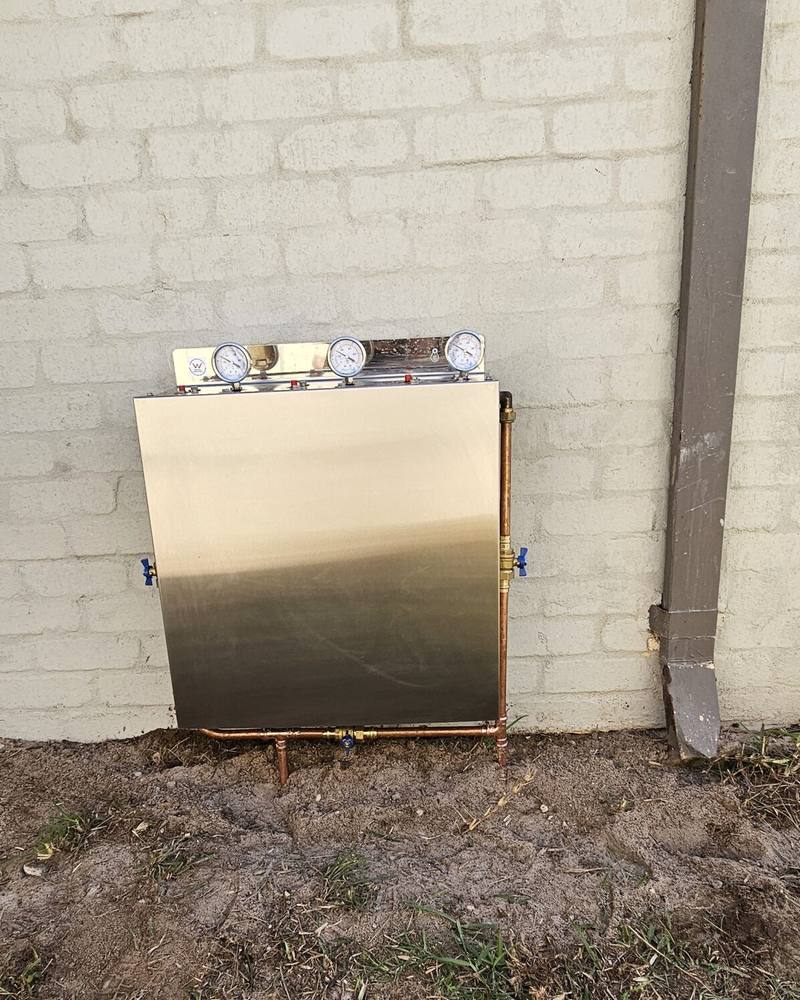 A stainless steel filter cover fitted to a cream brick wall
