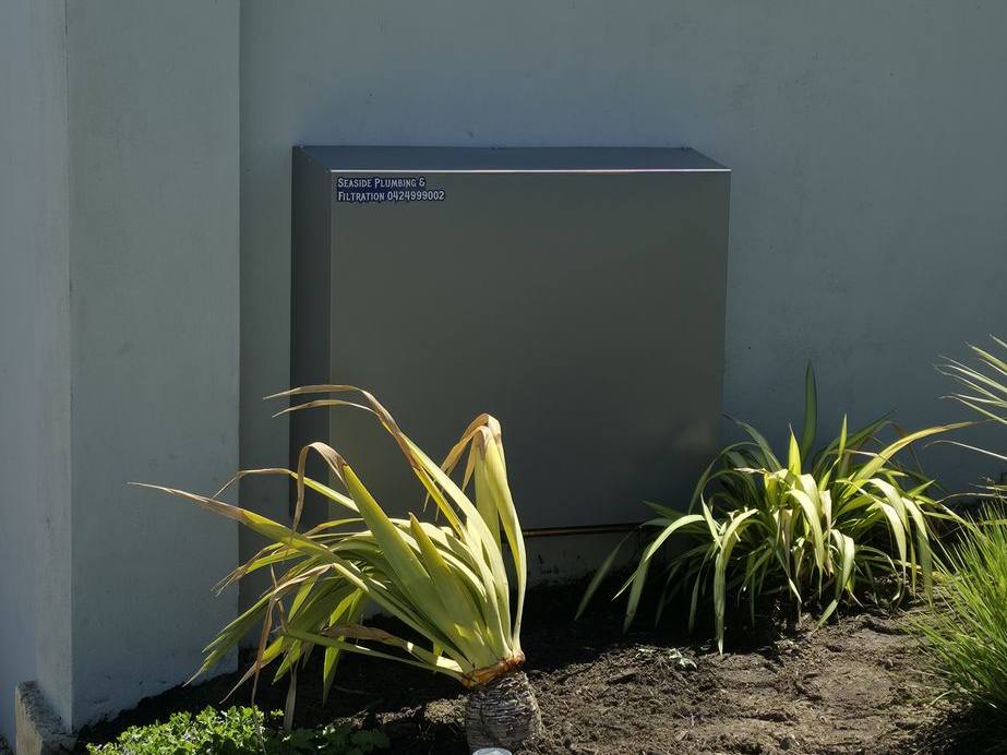A sage-grey filter cover on a rendered garden wall above a planted bed