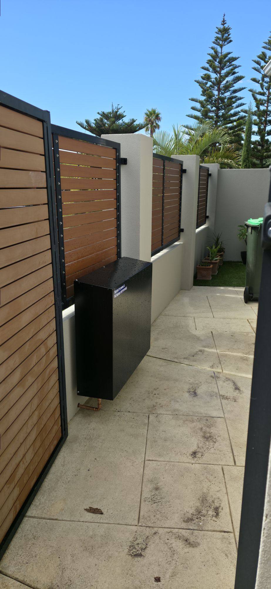 A dark filter cover beside timber slats along a paved side passage