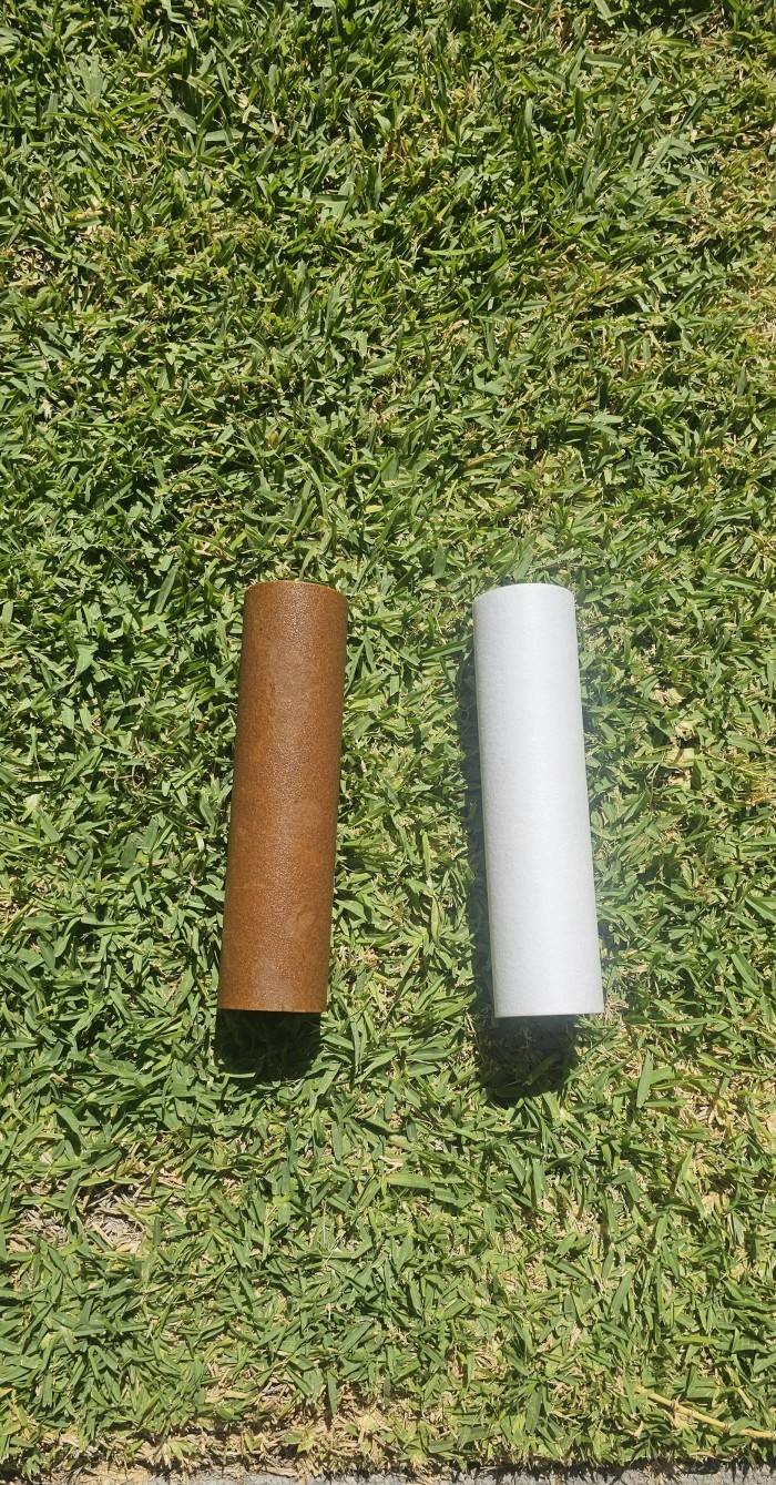 A used filter cartridge, stained brown, next to a clean new cartridge on grass