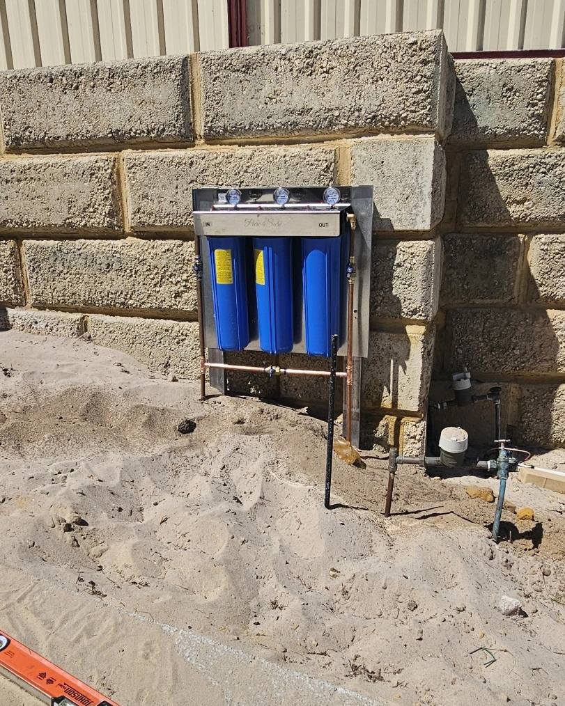 A whole-house filter being installed on a limestone wall, with a spirit level on the sand