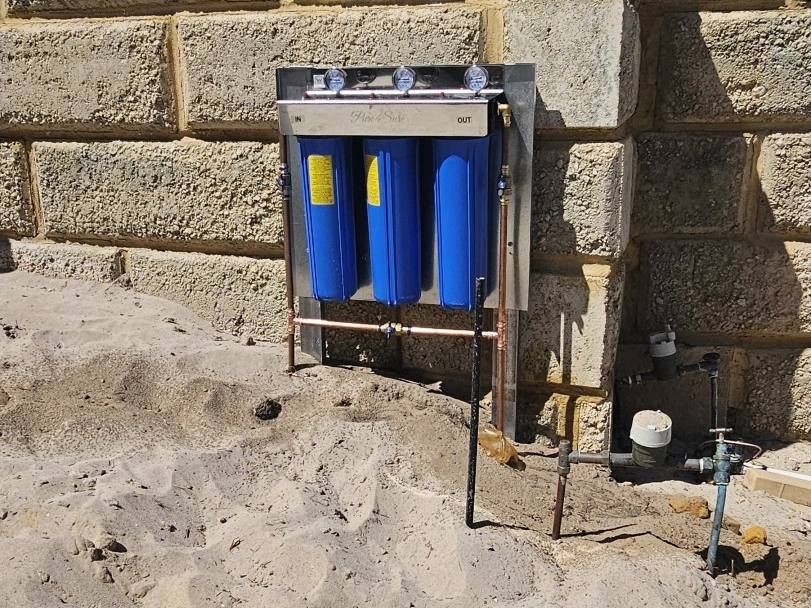 A whole-house filter being installed on a limestone wall, with a spirit level on the sand
