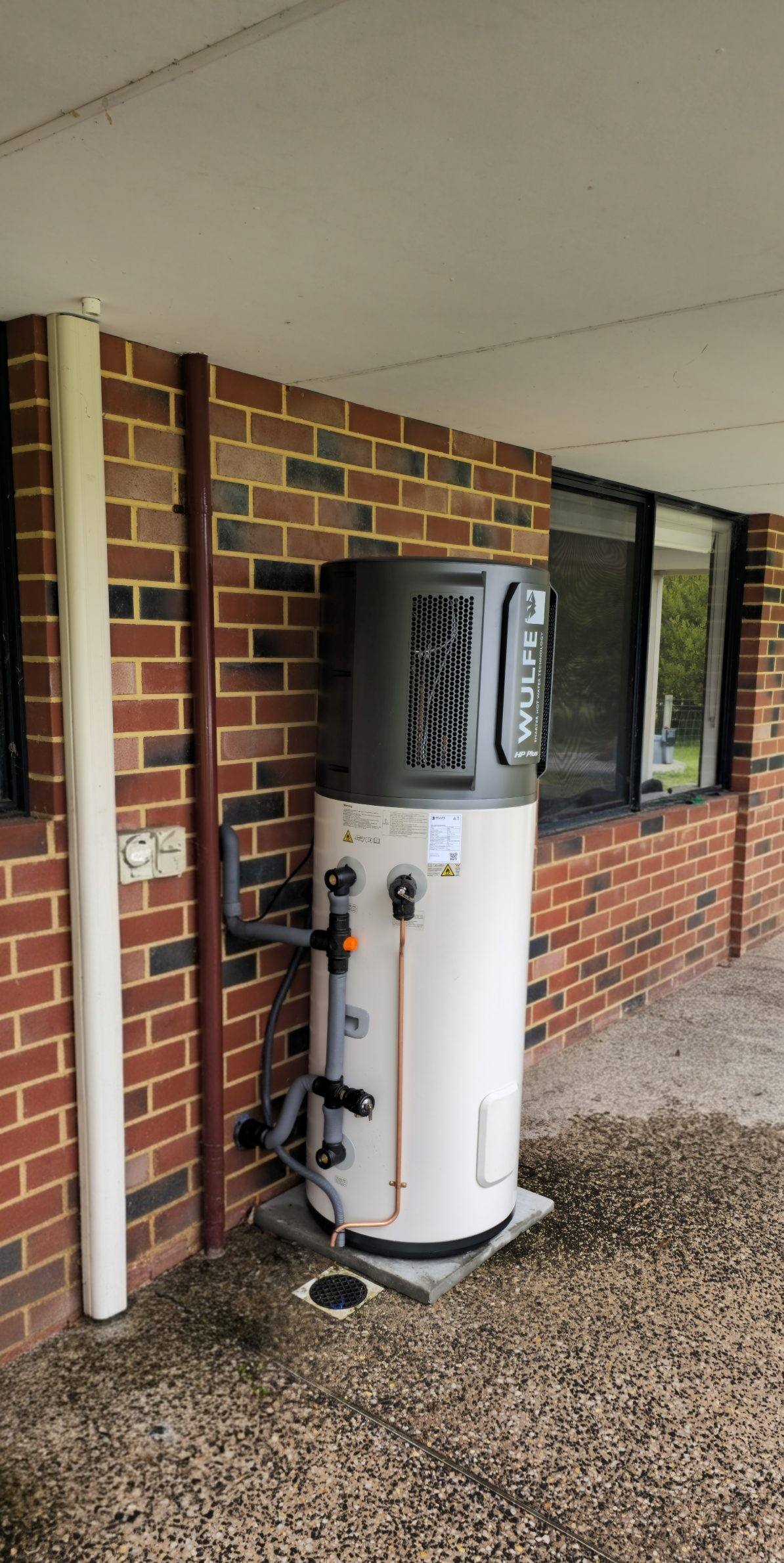 A heat pump hot water system installed beside a brick home