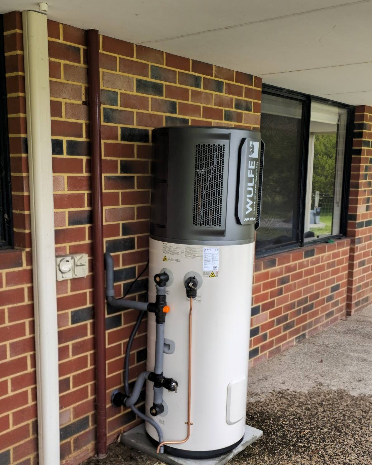 A heat pump hot water system installed beside a brick home