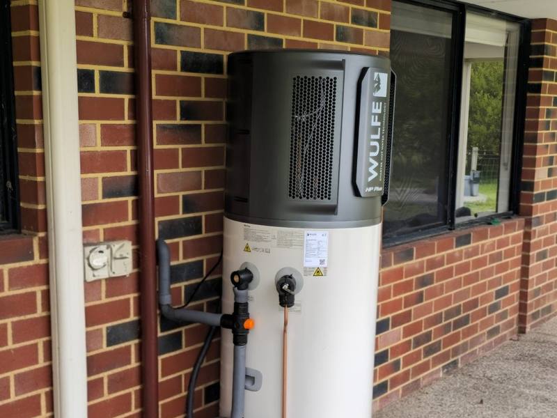 A heat pump hot water system installed beside a brick home