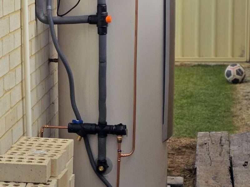 A replacement hot water unit with insulated pipework installed beside a brick wall