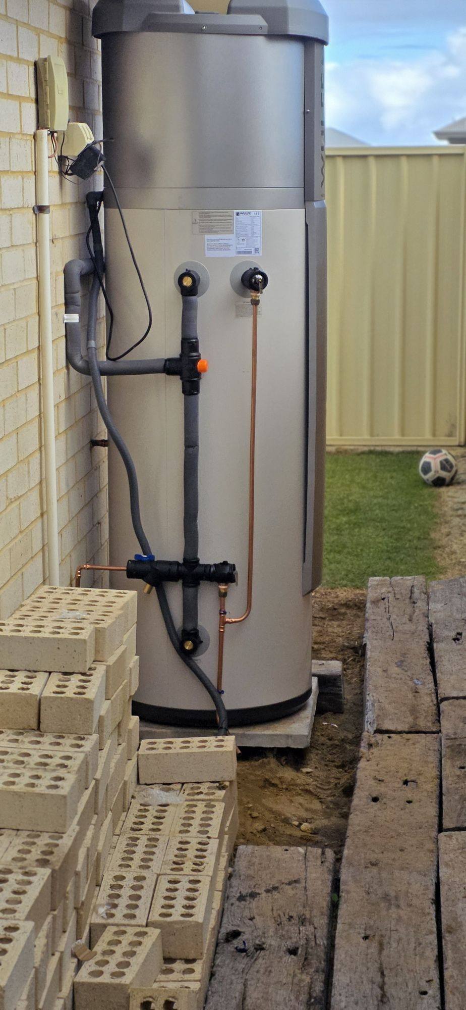 A replacement hot water unit with insulated pipework installed beside a brick wall