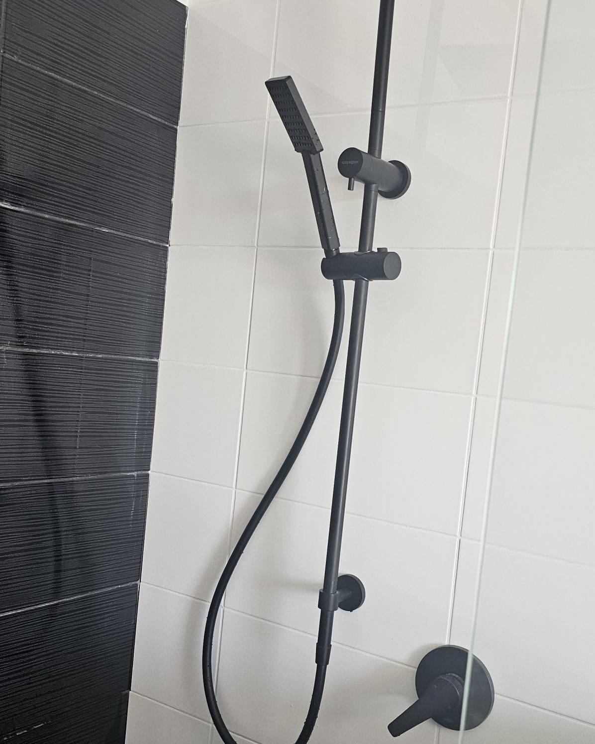 A matte black shower rail and mixer installed on white tiles