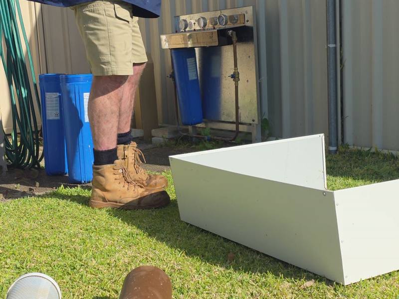 A tradesperson handling a filter cartridge beside opened filter housings, with a used cartridge on the lawn