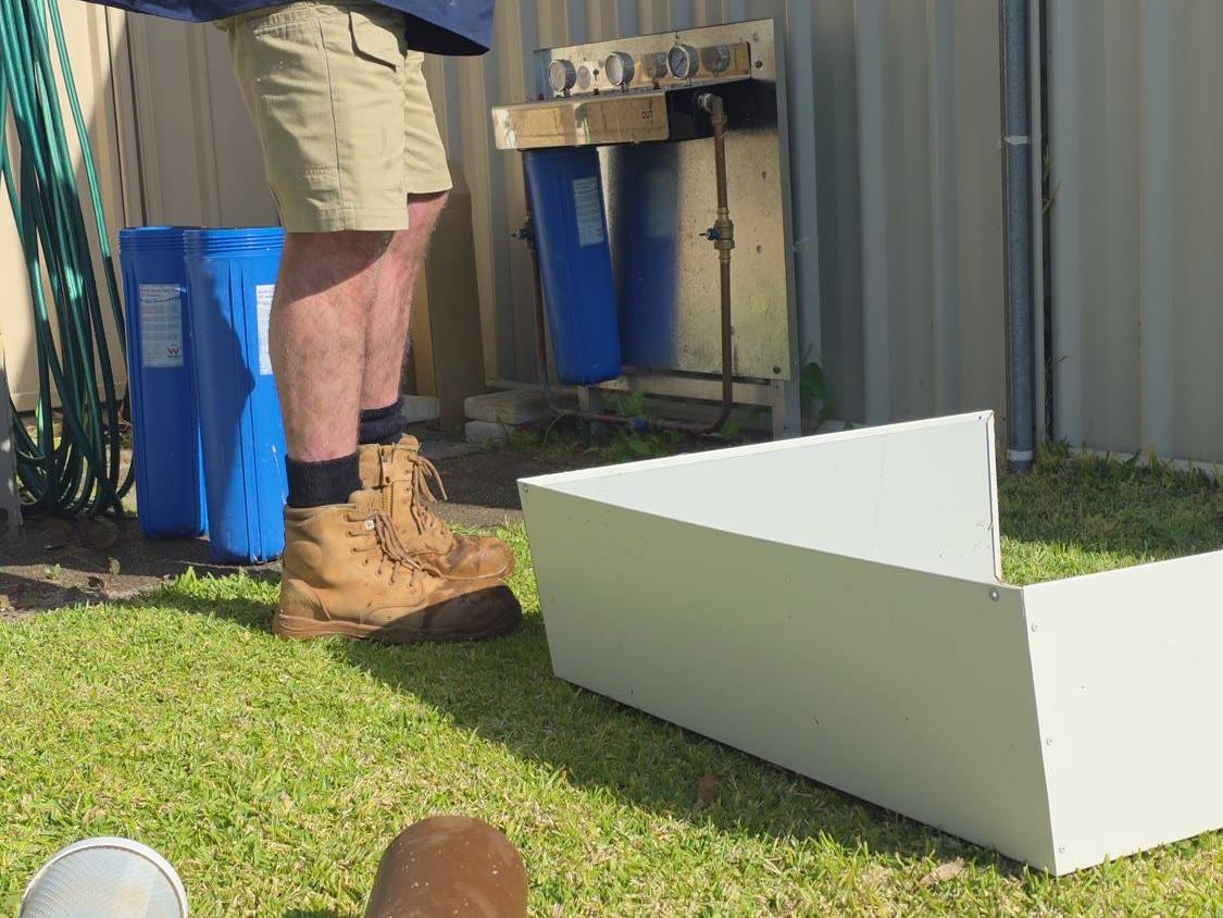 A tradesperson handling a filter cartridge beside opened filter housings, with a used cartridge on the lawn