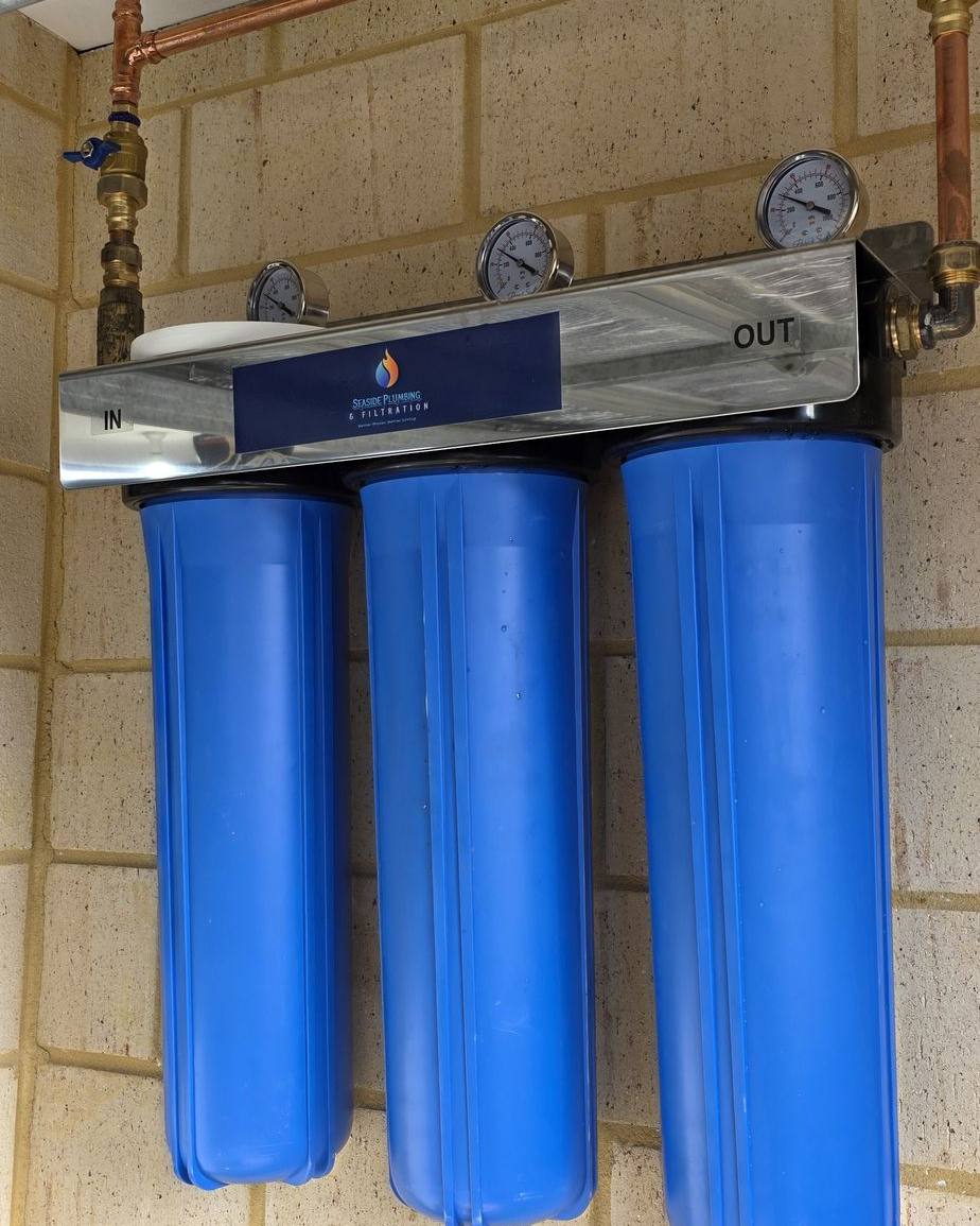 Close view of three blue filter housings, gauges and copper pipework beneath a garage door
