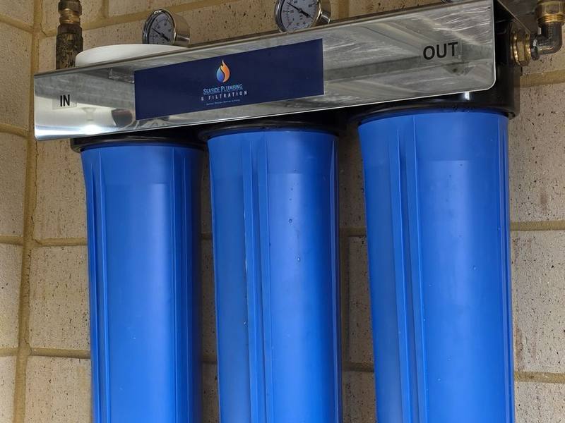 Close view of three blue filter housings, gauges and copper pipework beneath a garage door