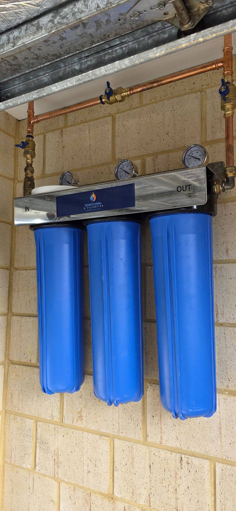 Close view of three blue filter housings, gauges and copper pipework beneath a garage door