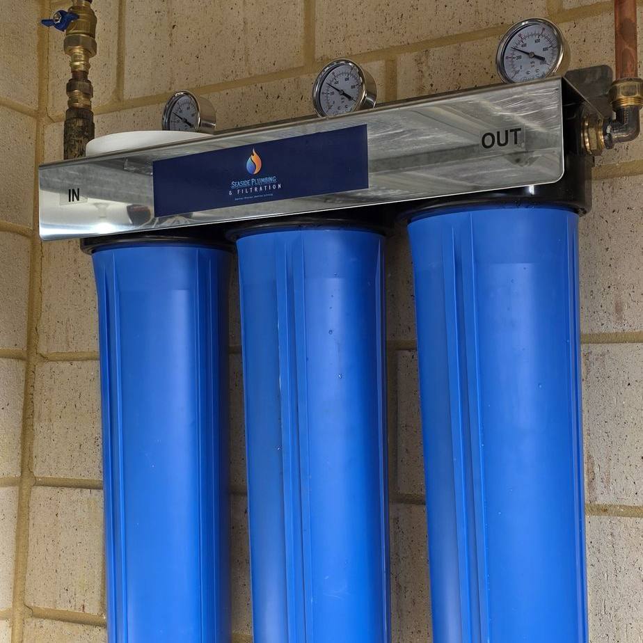 Close view of three blue filter housings, gauges and copper pipework beneath a garage door
