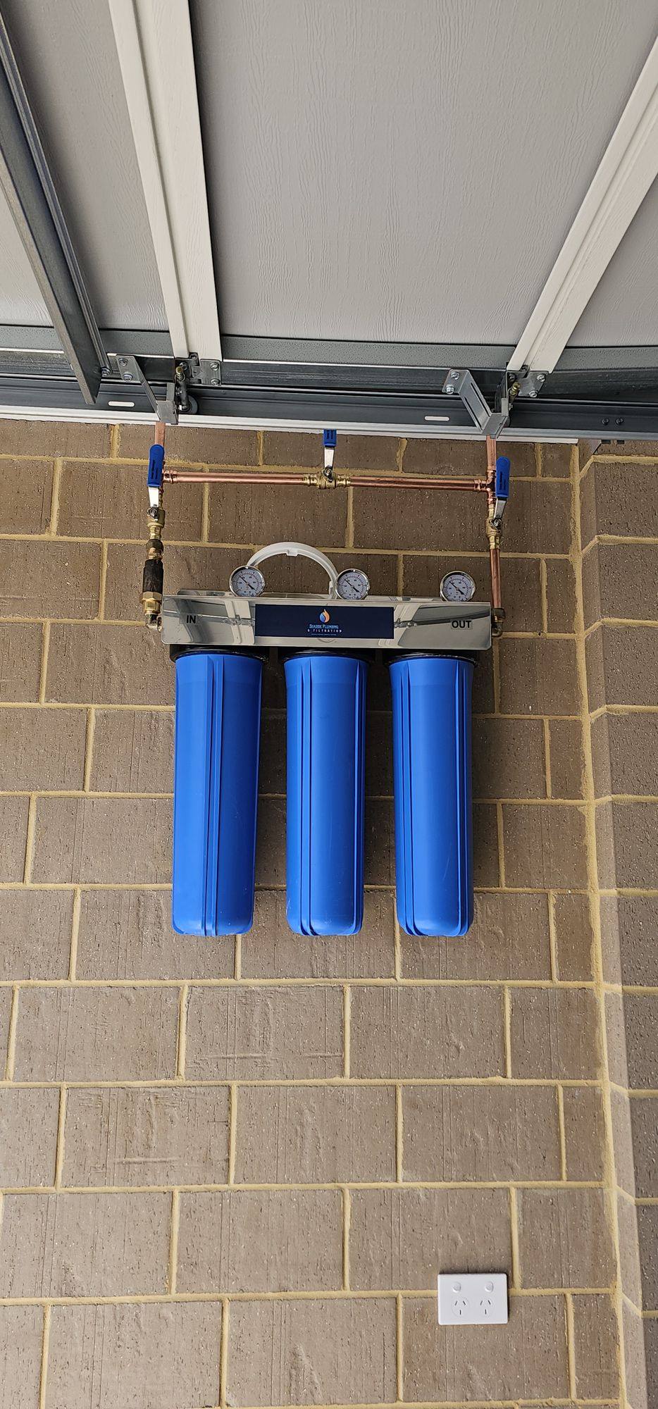 Three blue filter housings mounted on a brick wall beneath a raised garage door