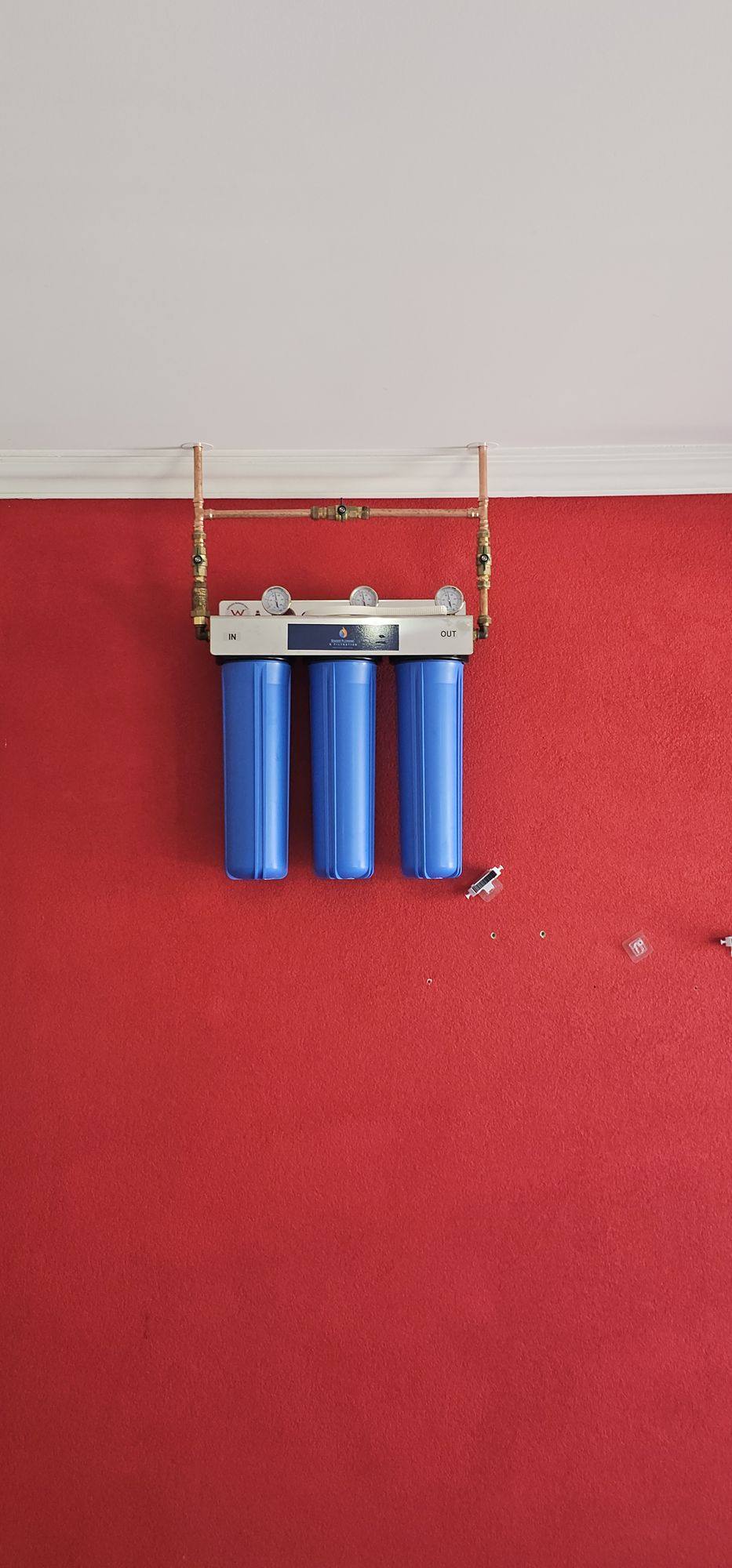 Three blue filter housings and copper pipes mounted on a red wall