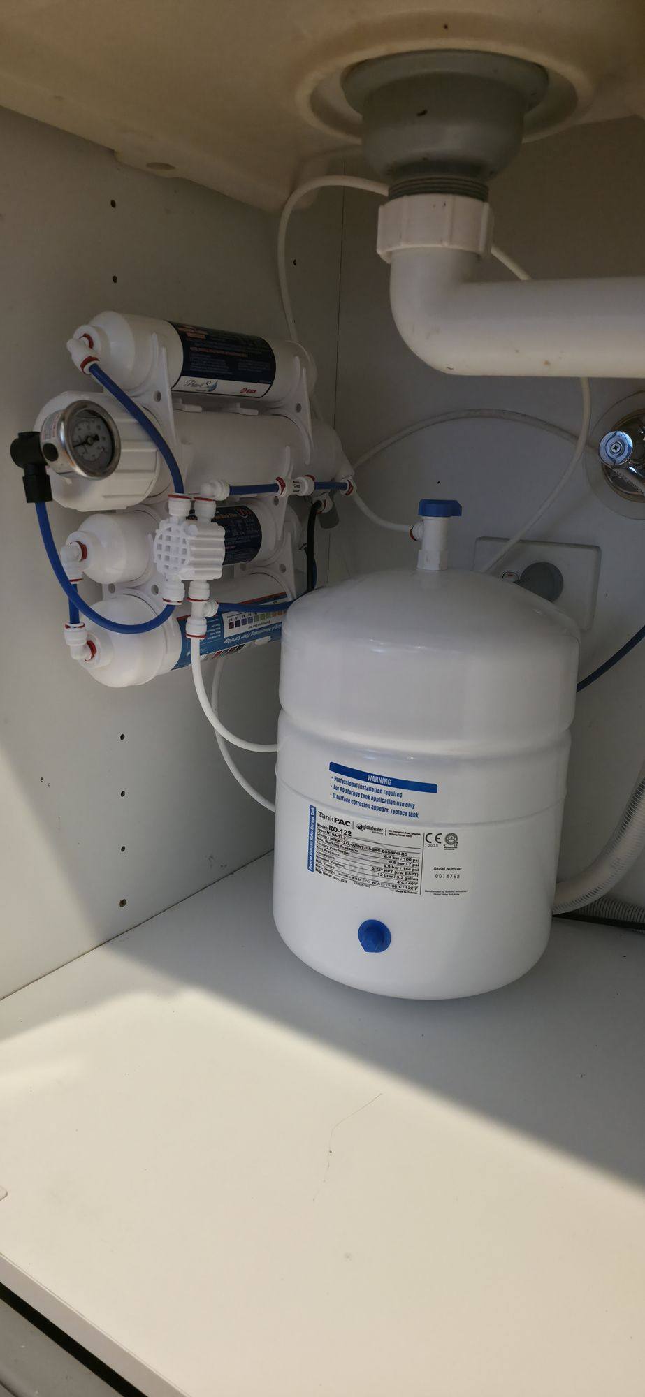 A reverse osmosis filter assembly and white storage tank in the cupboard beneath a kitchen sink